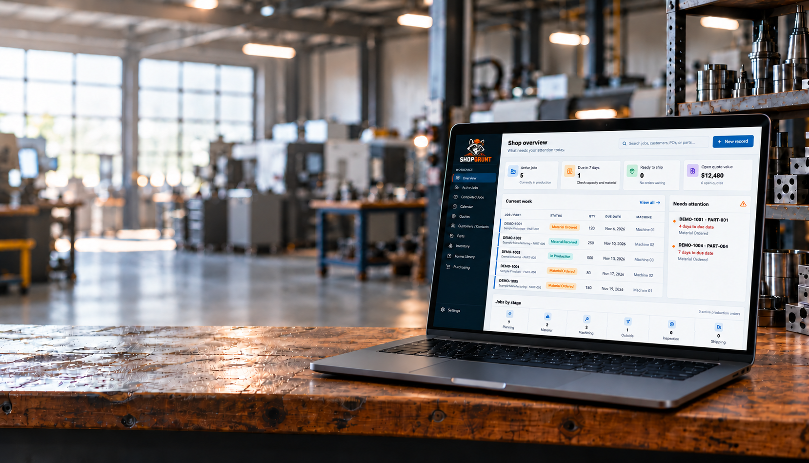 Laptop on a workshop bench showing an edited Shop Grunt dashboard with fictional demo data